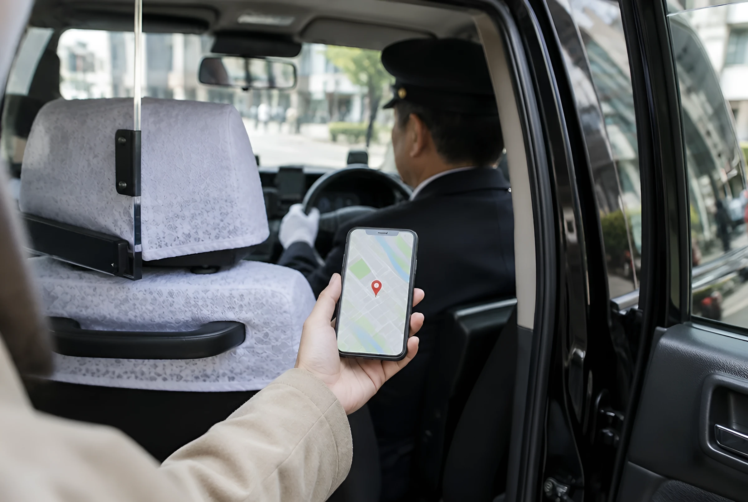 タクシーの後部座席から、地図のアプリを表示したスマホを運転手に見せる乗客の手