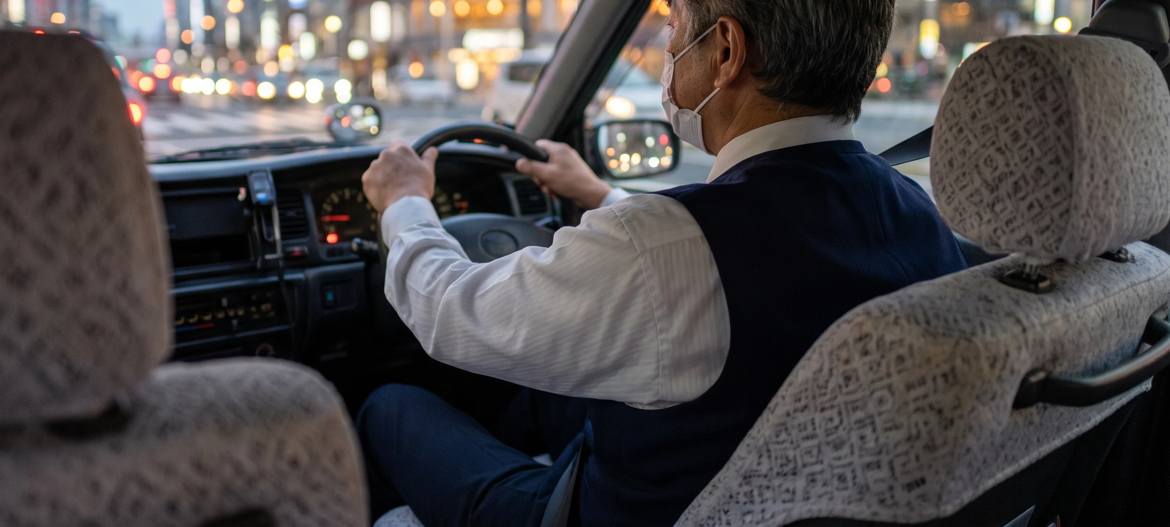 夕方の街を走るタクシーの車内。後部座席から見た運転席の乗務員